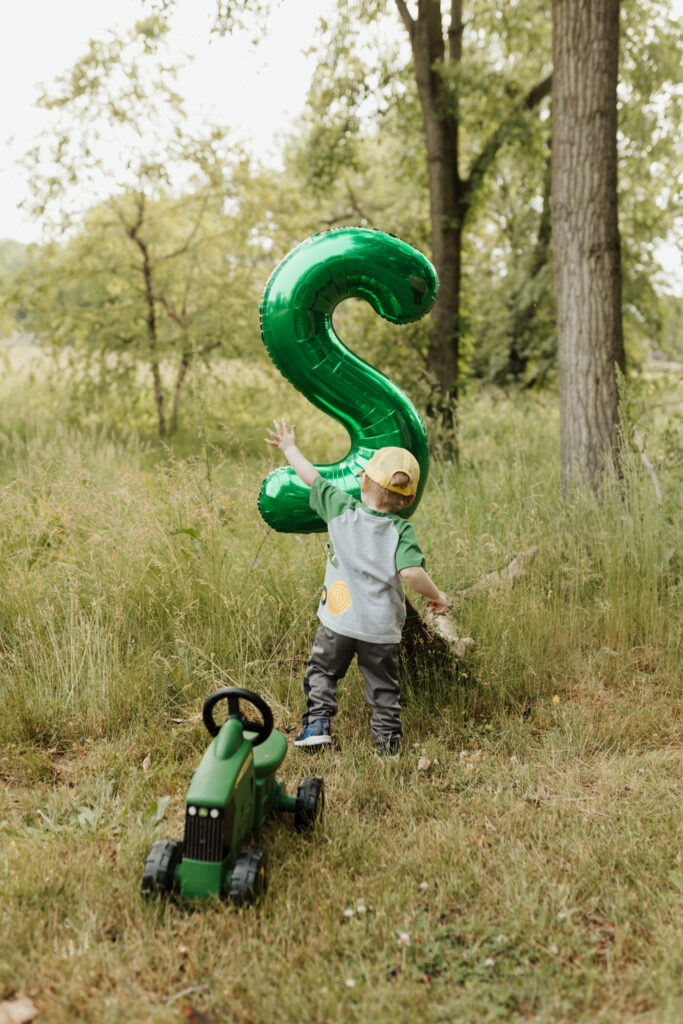 Two year old boy plays with his green balloon at his second birthday milestone photoshoot