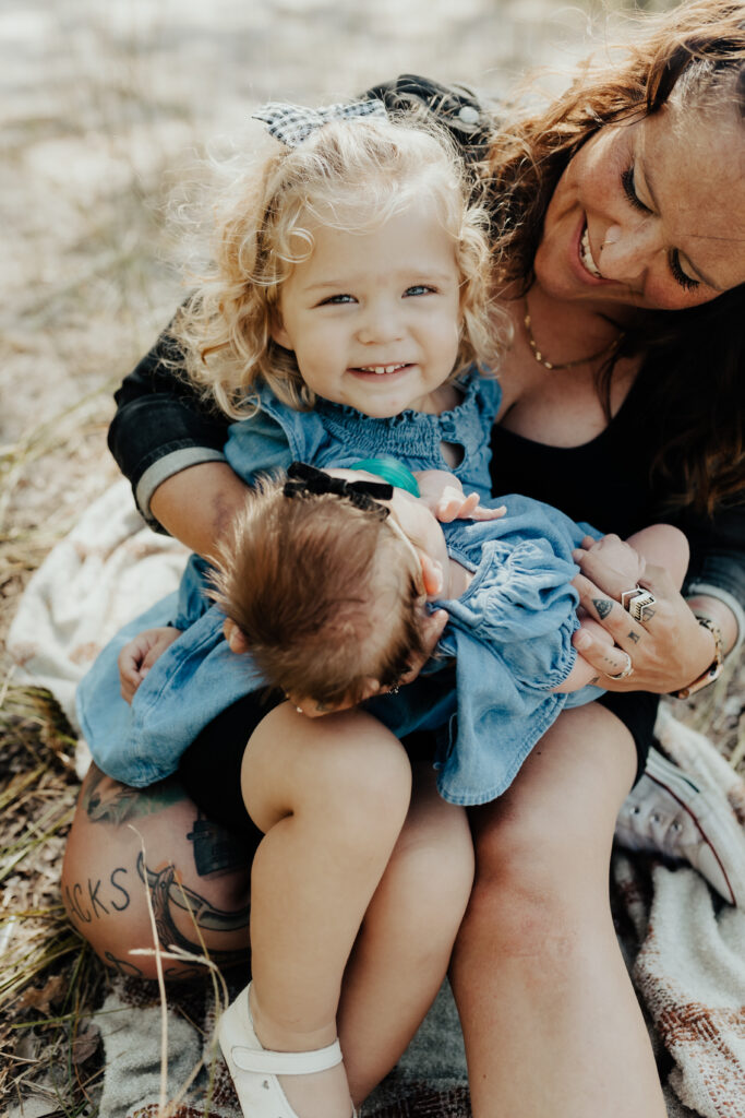 mother, toddler and newborn at the beach, sitting together and smiling